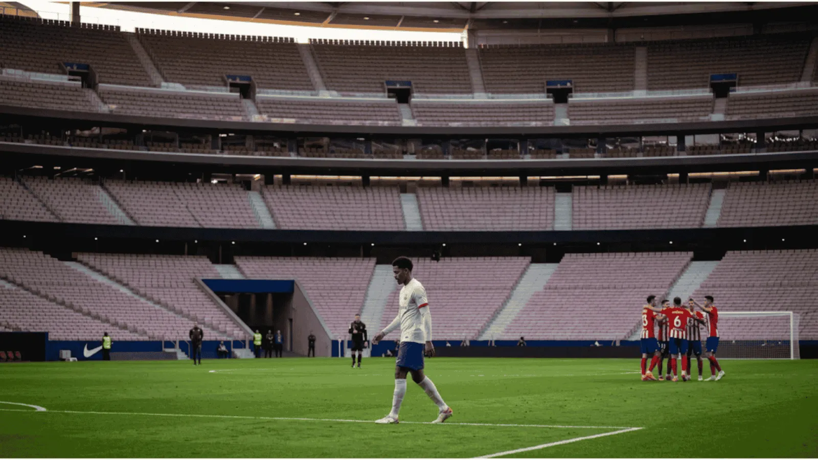 A candid, wide-angle photojournalism image at a massive, near-empty stadium after the final whistle. In the foreground, a dejected Barcelona player walks alone toward the tunnel, while in the far